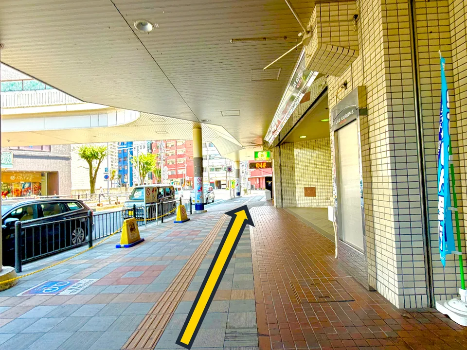 駅前の建物沿いにある屋根付き歩道を直進する黄色い矢印