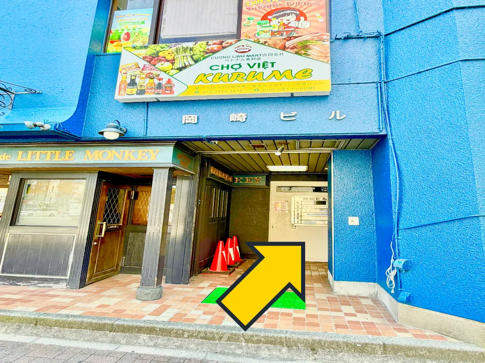青い外壁の岡崎ビル入口を示す黄色い矢印